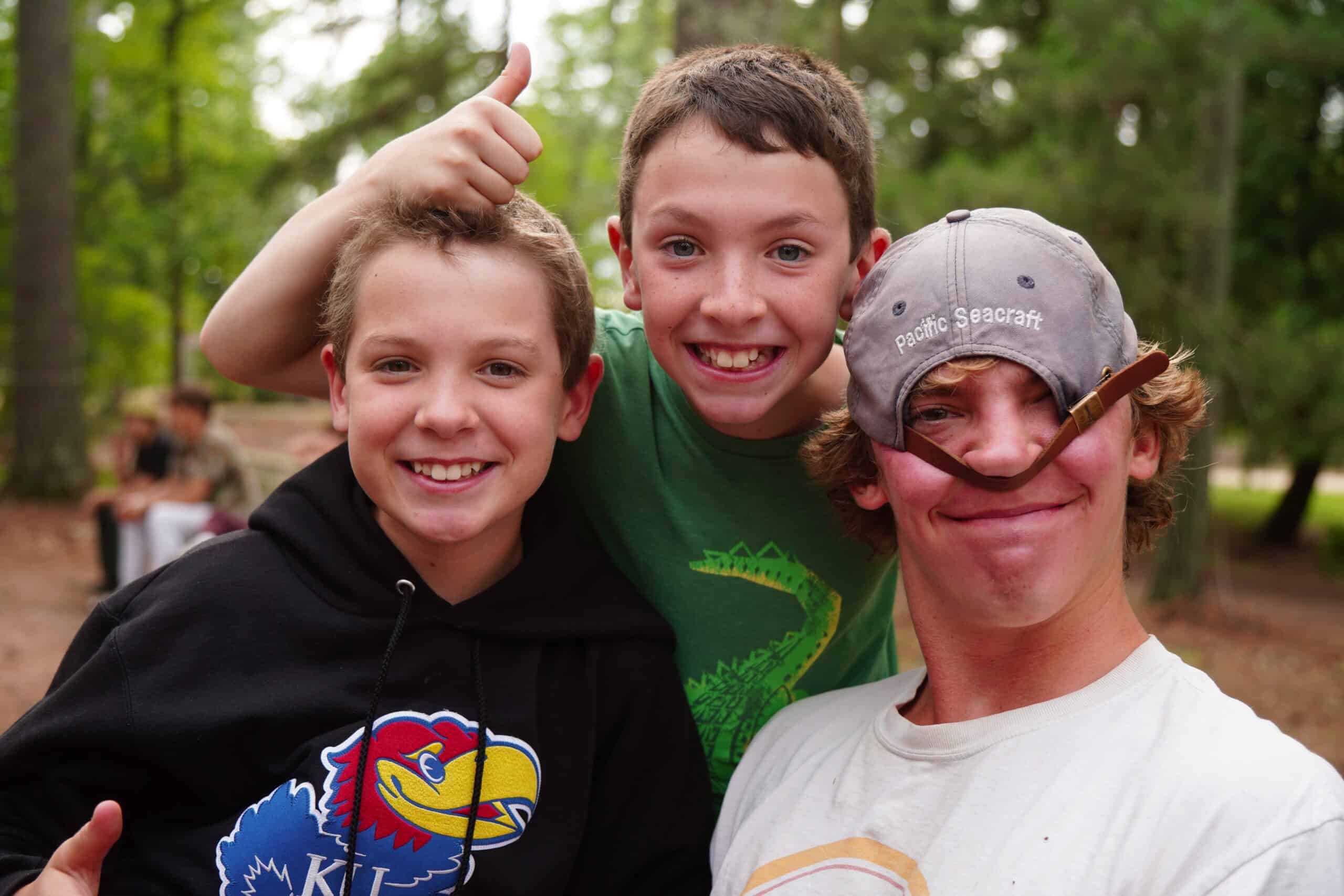 two boys and one counselor with a goofy hat smiling.
