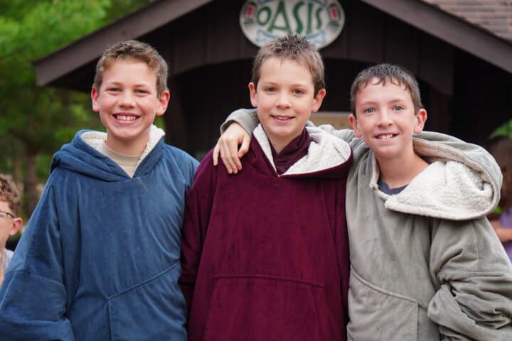 three boys at summer camp smiling with hoodies.