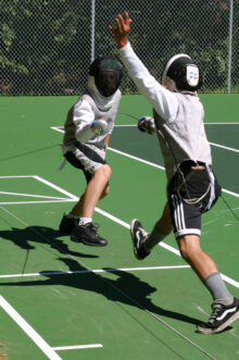 two boys fencing on a tennis court.
