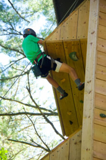 boy in green shirt climbing on climbing tower outdoors.