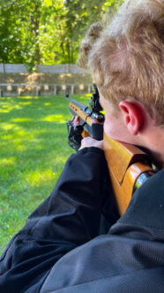 boy aiming down the sights of a rifle on a range.