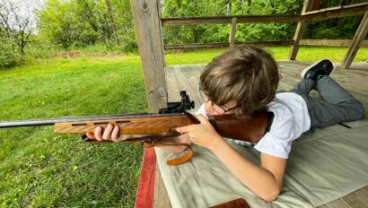 boy aiming down the sights of a rifle on a range.