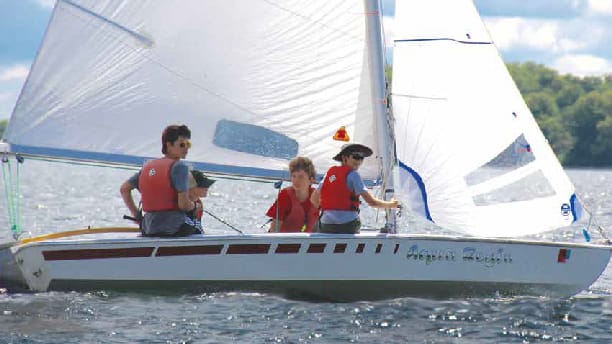 four boys sailing a sailboat on a lake.