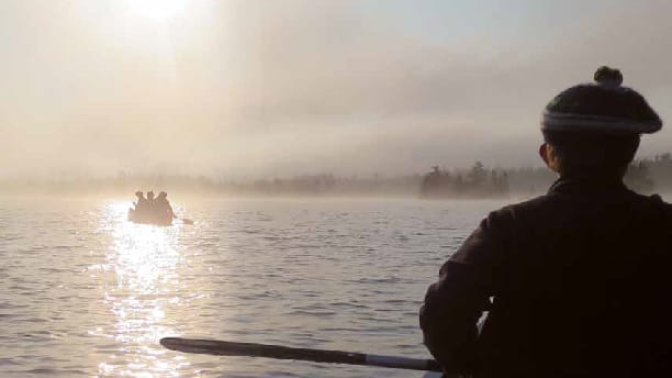 two canoes on a lake while the sun is going down.