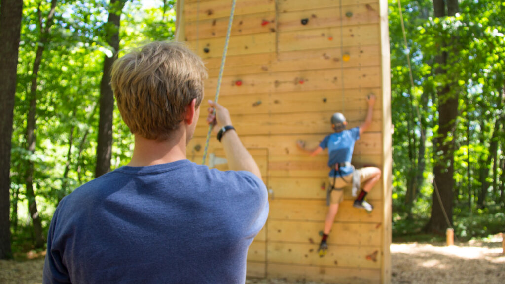 climber on a climbing wall with a belayer in the foreground.