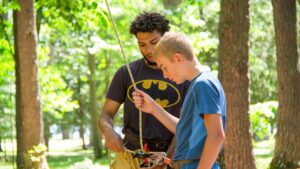 older teen showing a boy how to use climbing gear.