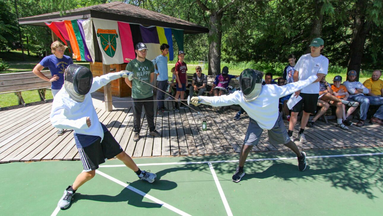 two boys fencing in front of crowd outdoors.