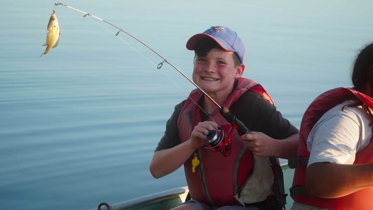 boy smiling with fish he caught on lake.
