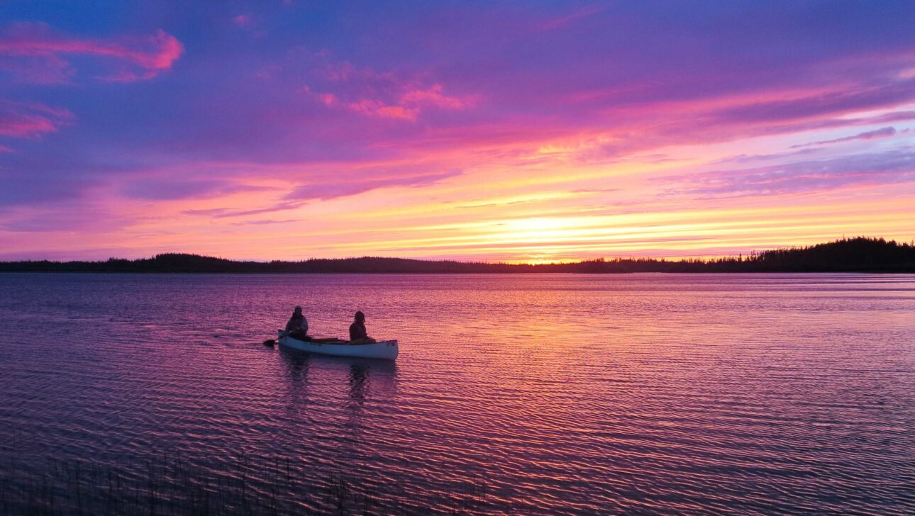 canoe on lake with purple rainbow colored sky.