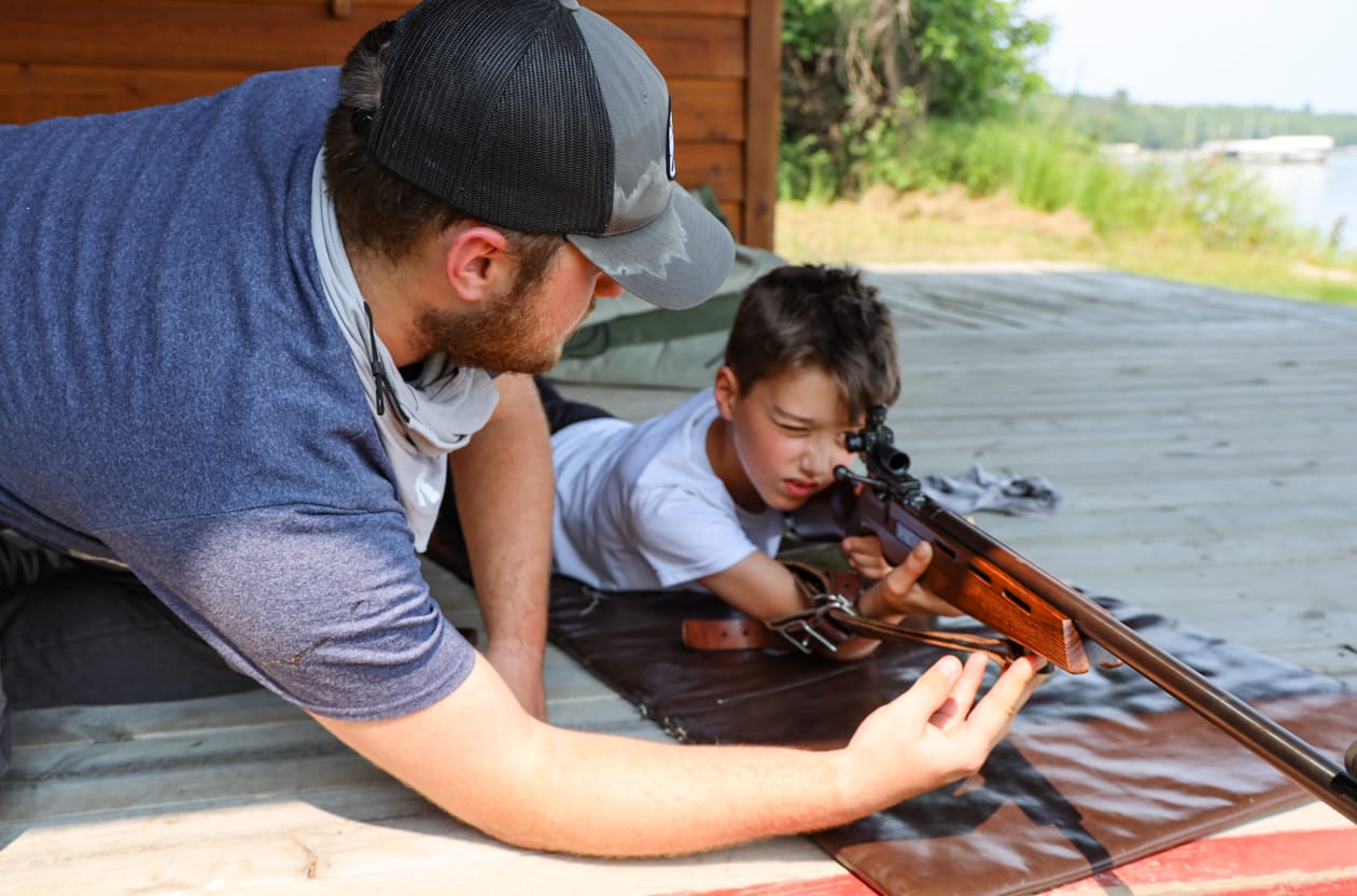 man teaching boy how to shoot rifle.