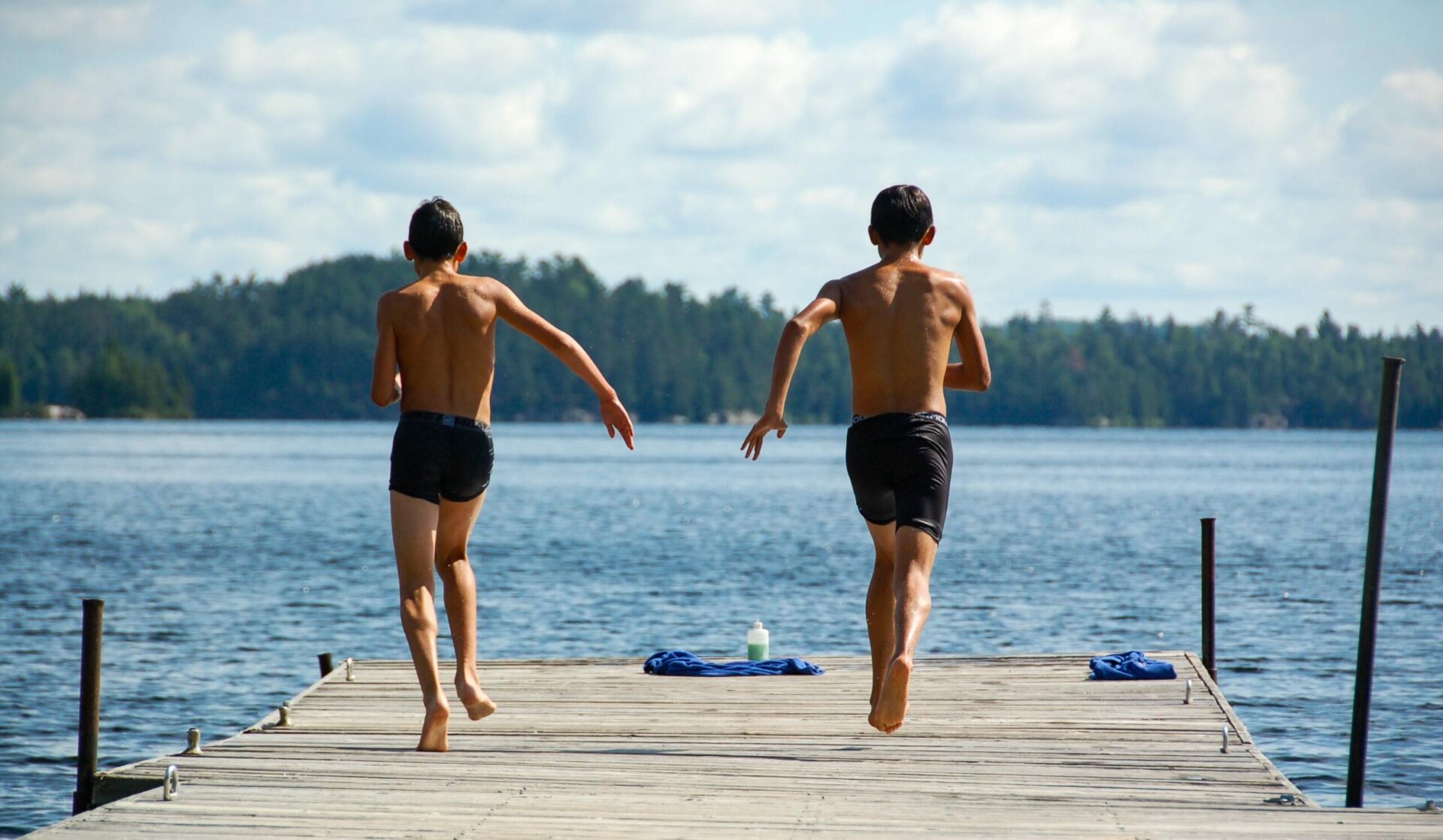 two boys running off a dock towards the water.