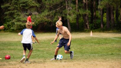 shirtless boy juking another player with a soccer ball.