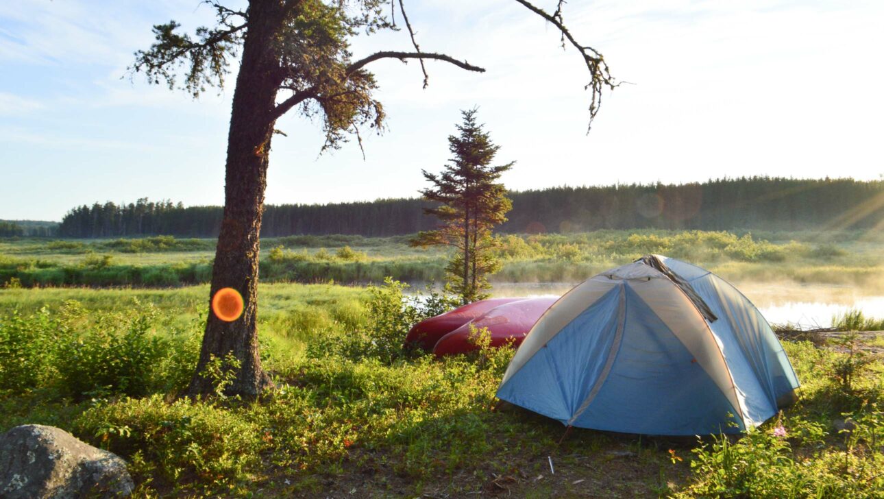 tent and canoe set up next to river.