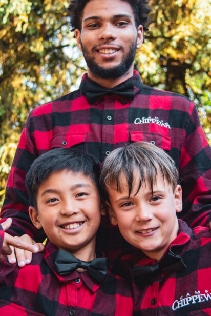 two boys standing in front of a teen boy with red checked shirts and black bow ties.