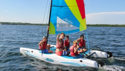 boy showing thumbs up sign on sailboat with other boys.