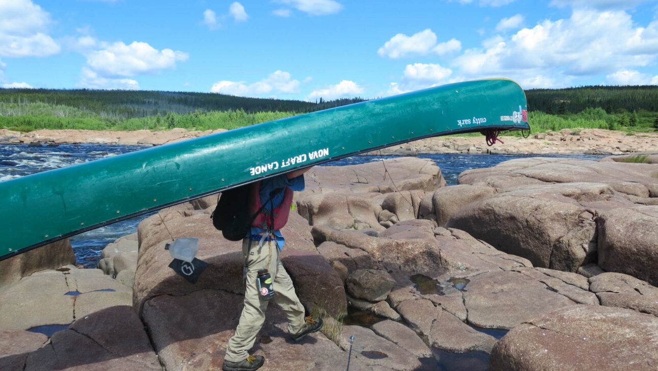 boy carrying a canoe on his head over rocks.