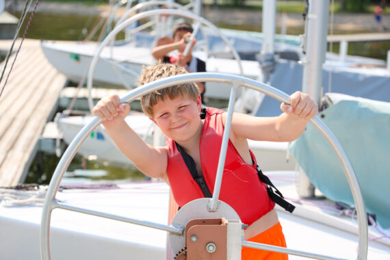 boy hanging under a wheel on a boat.