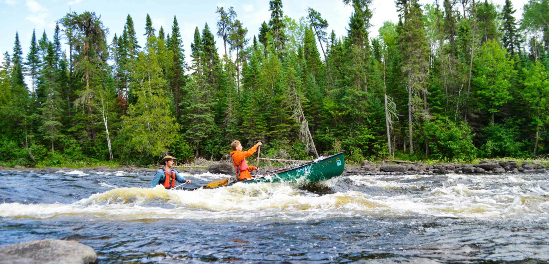 two boys canoeing over rapids.