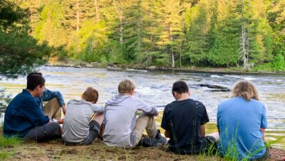 boys resting next to a river on an outdoor trip.