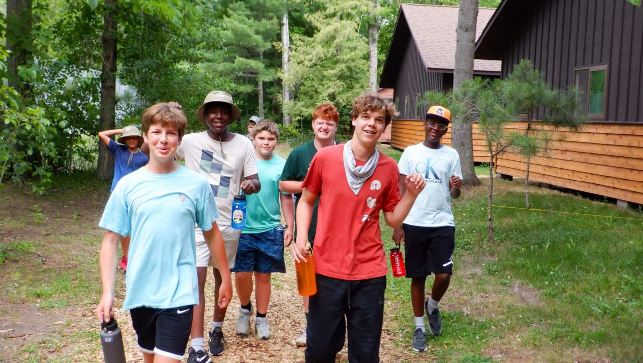 group of boys walking outside next to wood cabins.