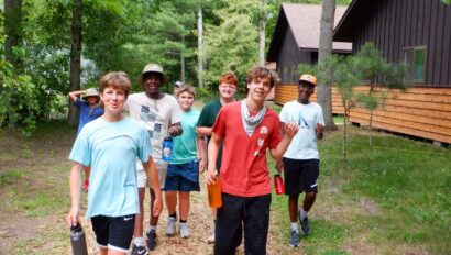 group of boys walking outside next to wood cabins.