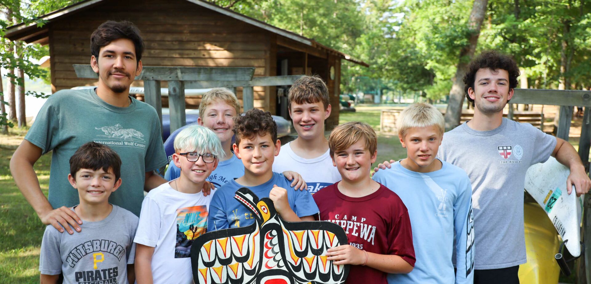 group boys smiling and holding a colorful sign in the shape of a bird at a camp.