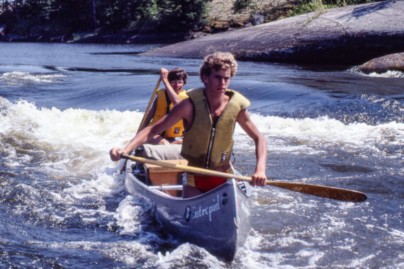 old photo of two boys canoeing through rapids.