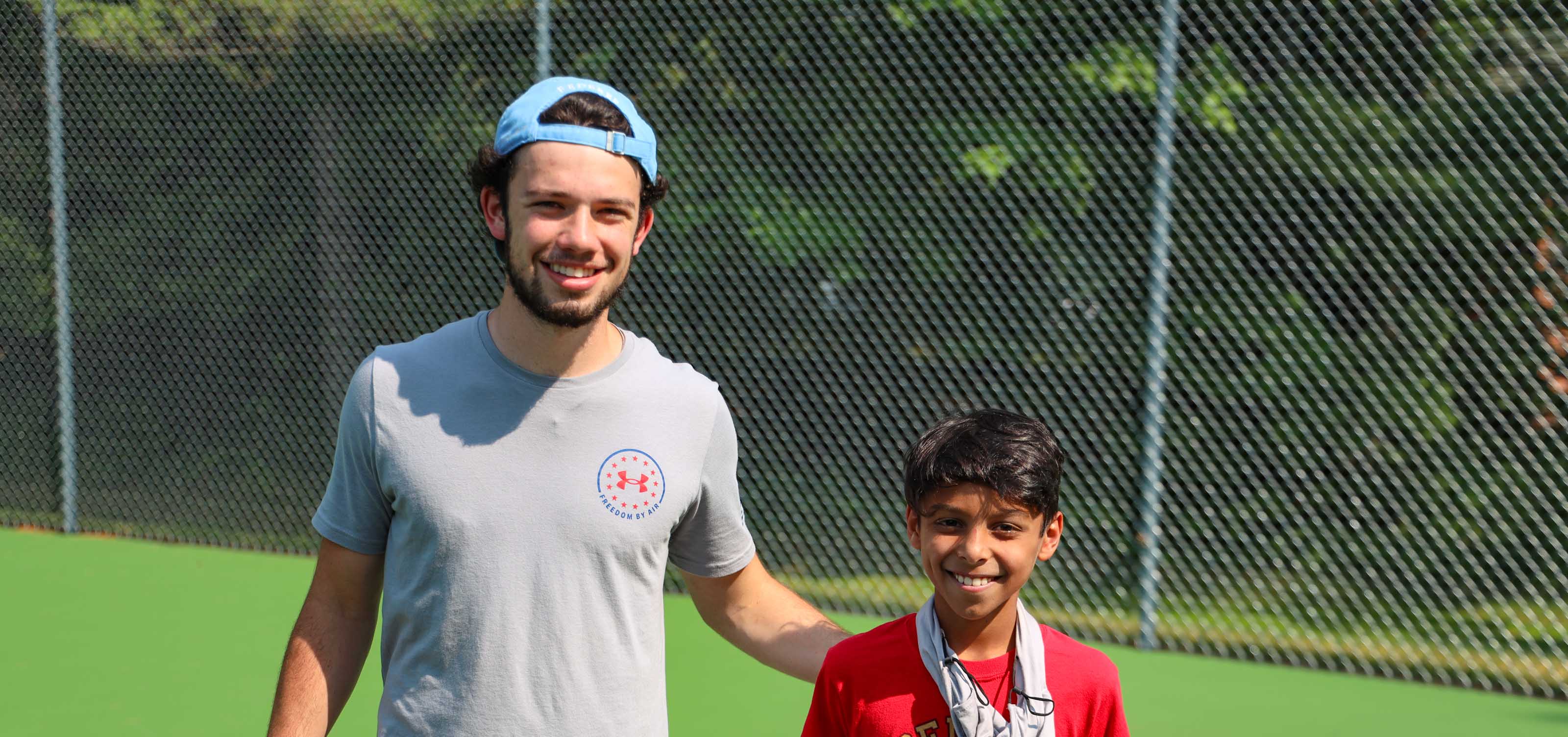 camp counselor and boy on tennis court smiling for camera.