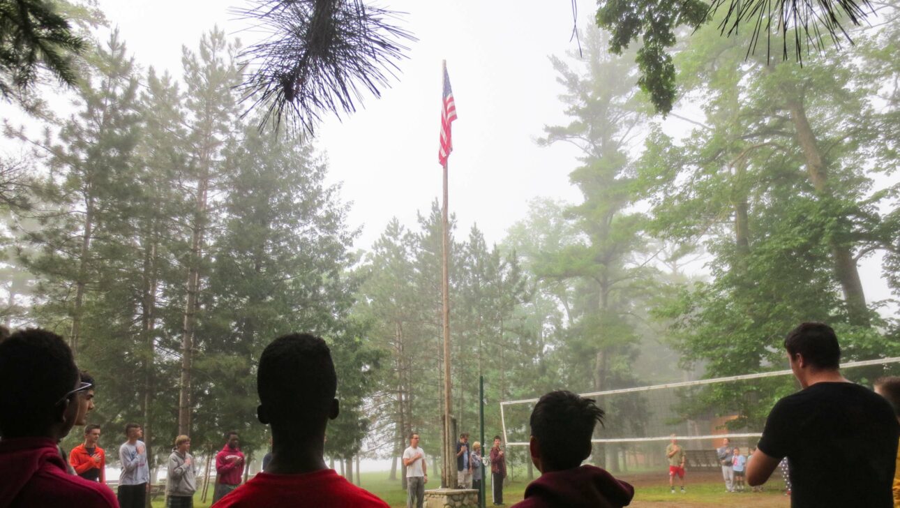 boys standing around a flag being raised during a misty morning.