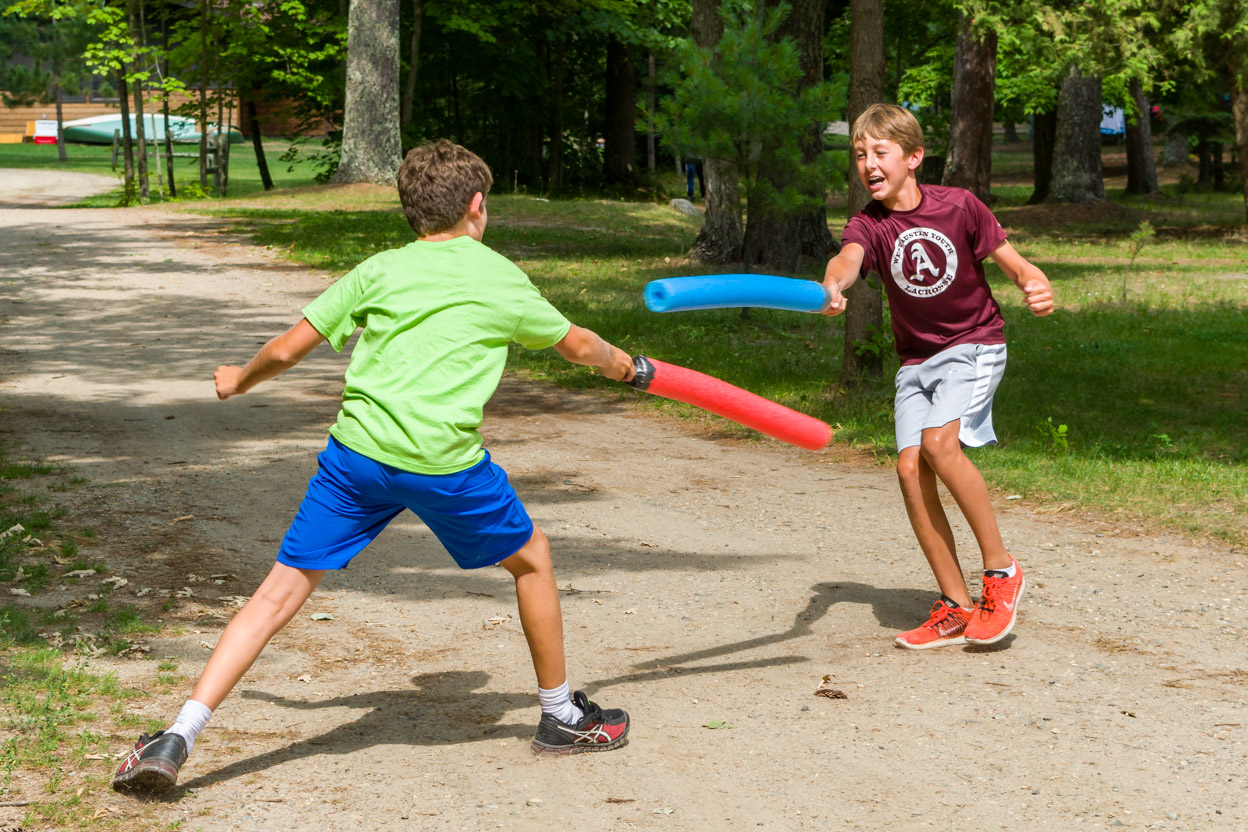 two boys sword fighting outdoors with foam swords.