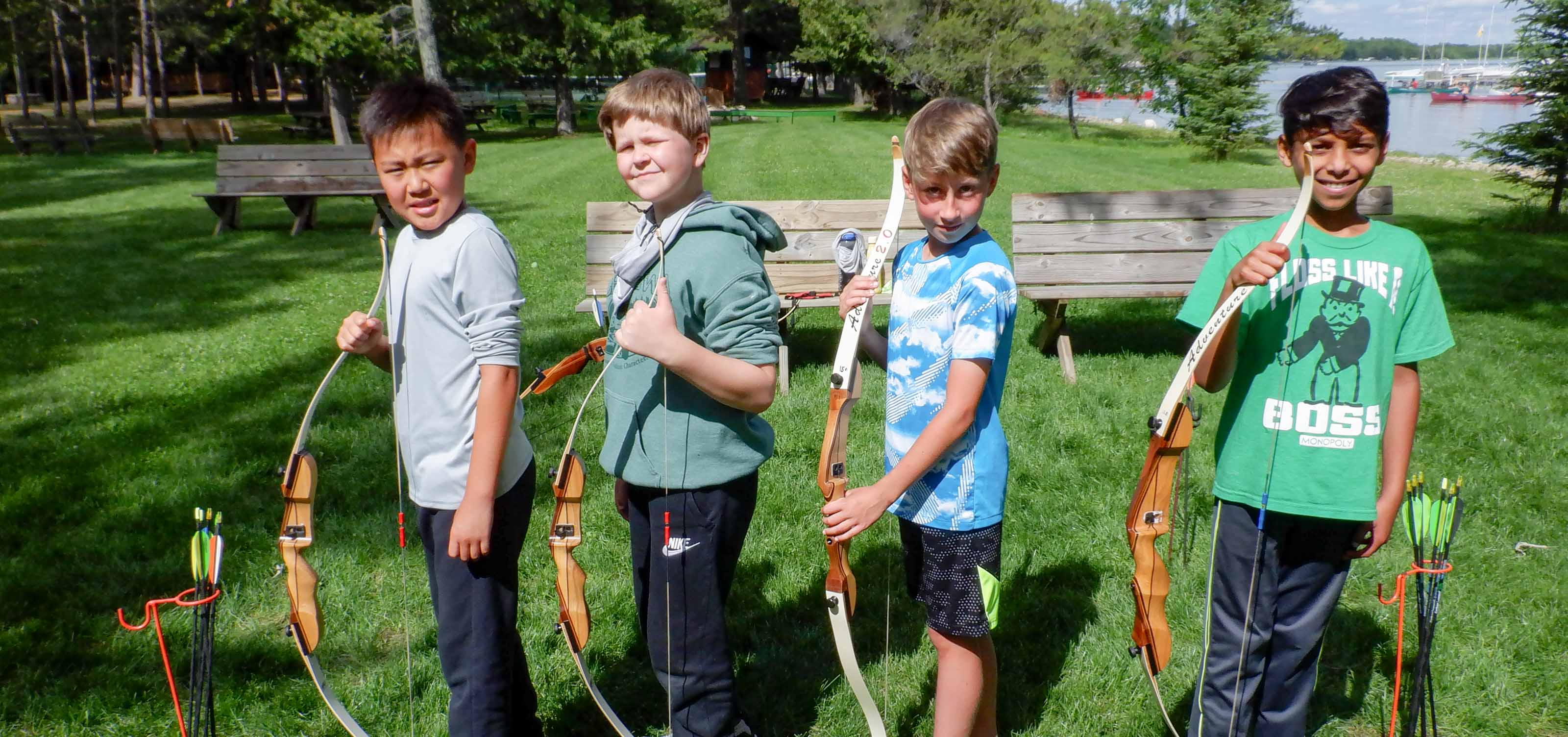 four boys with bows and arrows squinting in the sun.