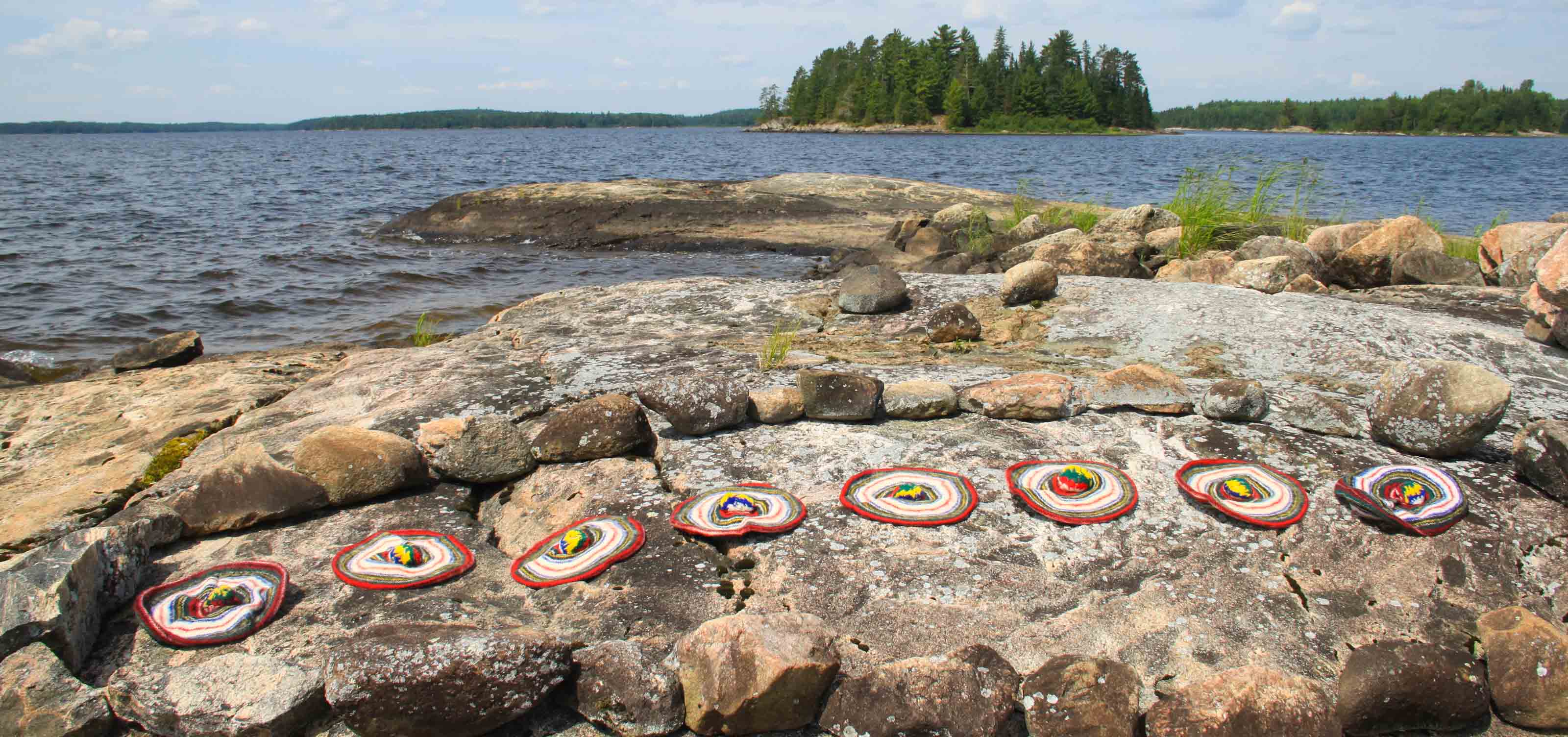 colorful felt hats drying in the sun on a rock next to a lake.