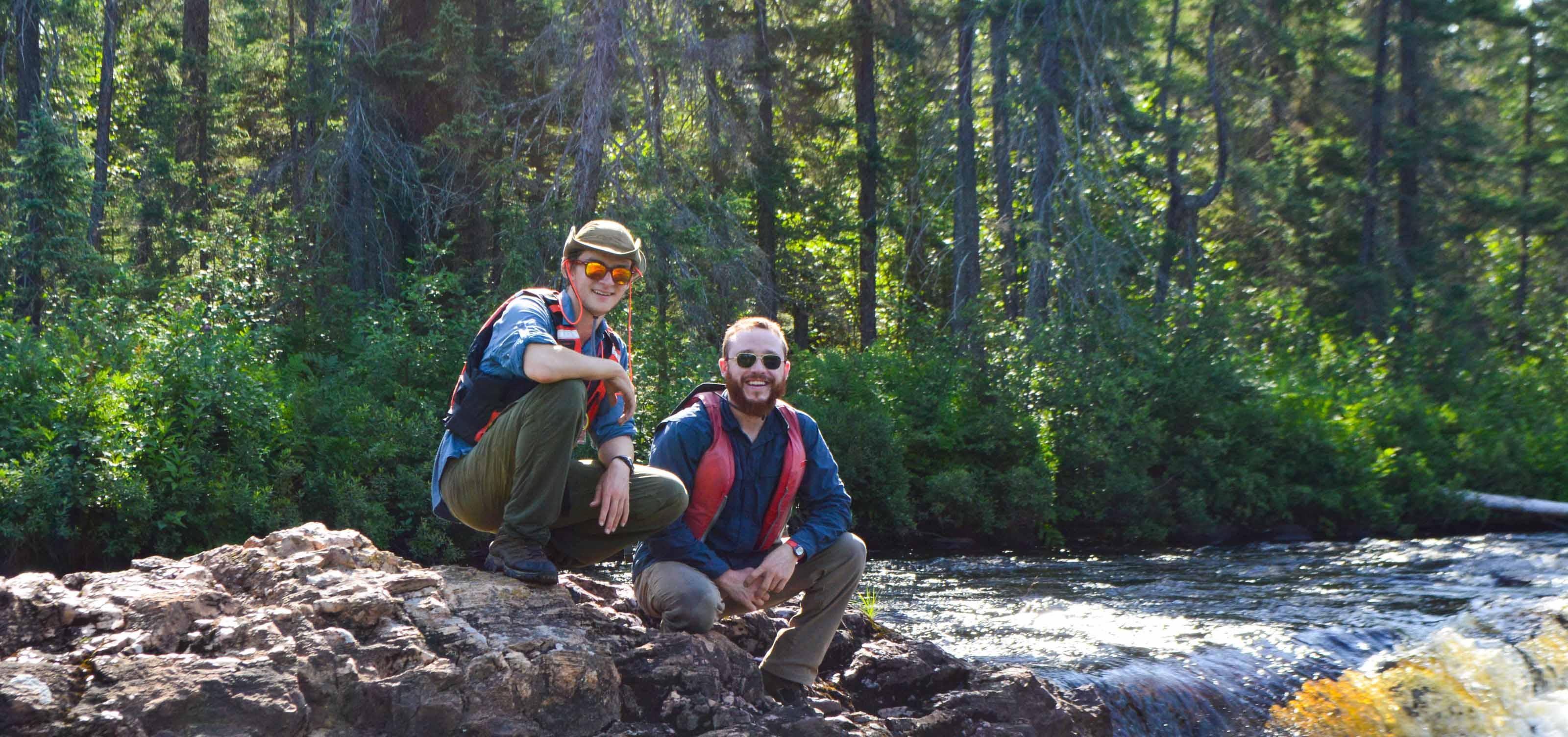 hikers sitting on rock next to river rapids.