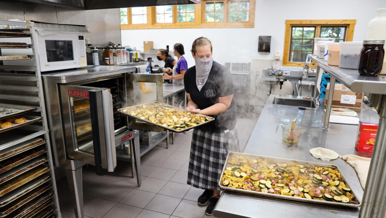 woman pulling baking tray out of oven in commercial kitchen.