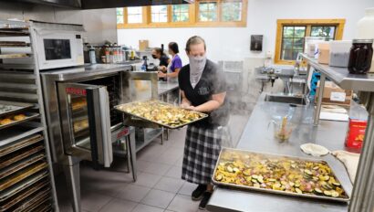 woman pulling baking tray out of oven in commercial kitchen.