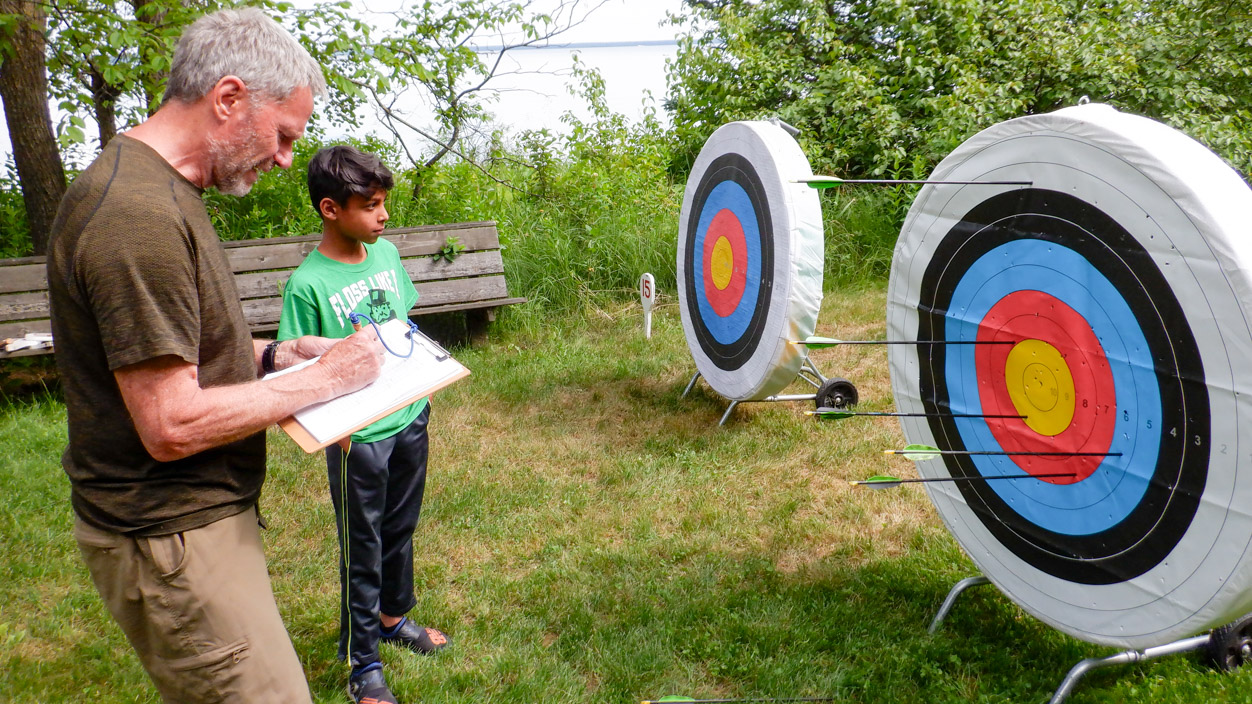 man scoring an archery target with a boy.