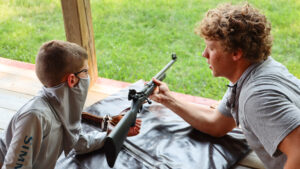camp counselor showing a boy how to shoot a rifle.