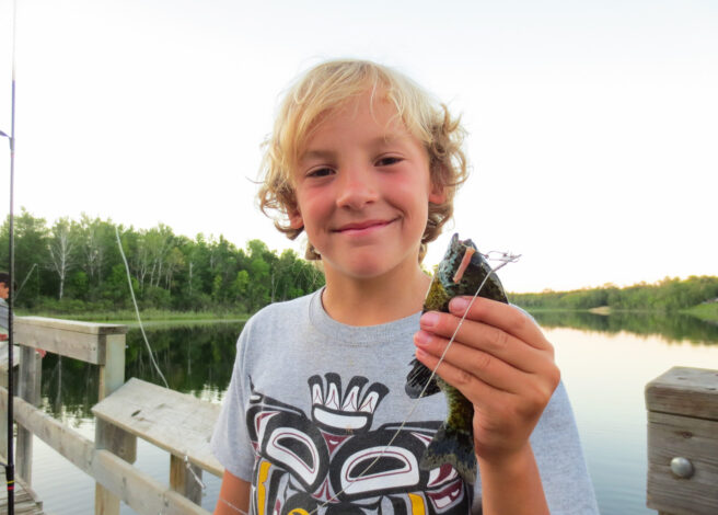 boy on dock smiling and holding a fish.