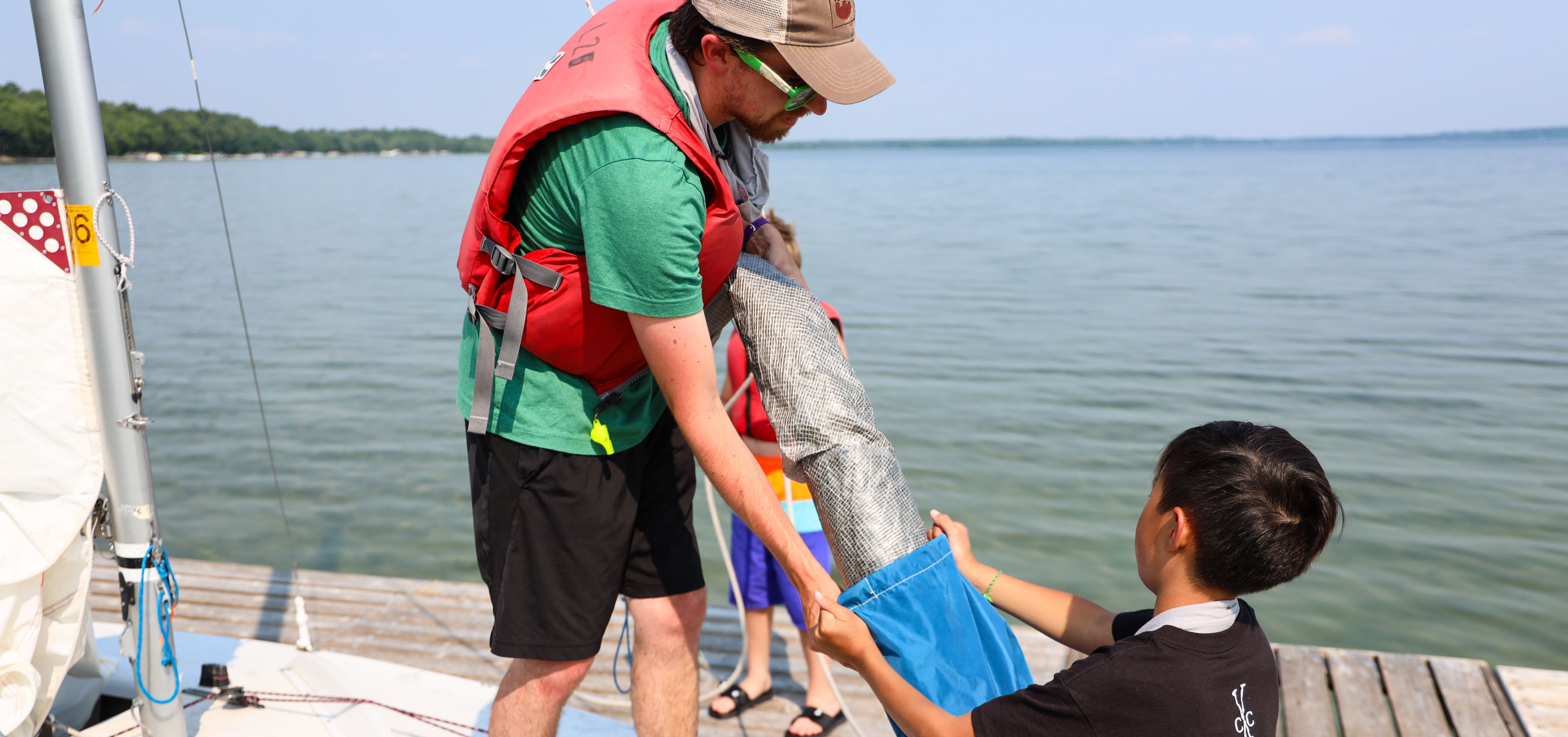 camp staff member putting away sail on boat with young boy.