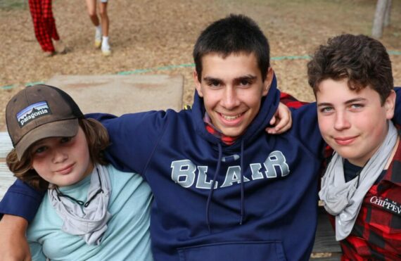 three boys next to eachother on a bench outdoors smiling.