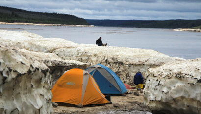 two tents next two a river amongst snow piles.