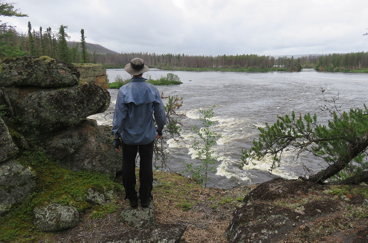 person overlooking rapids and trees in the distance.