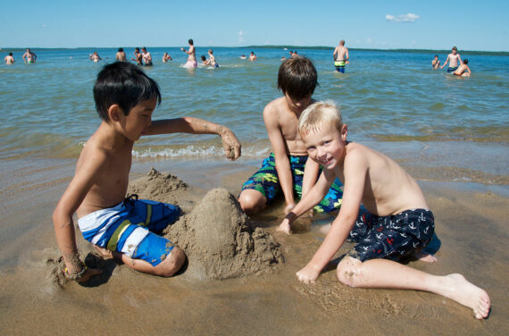 three campers building sandcastles by the lake.