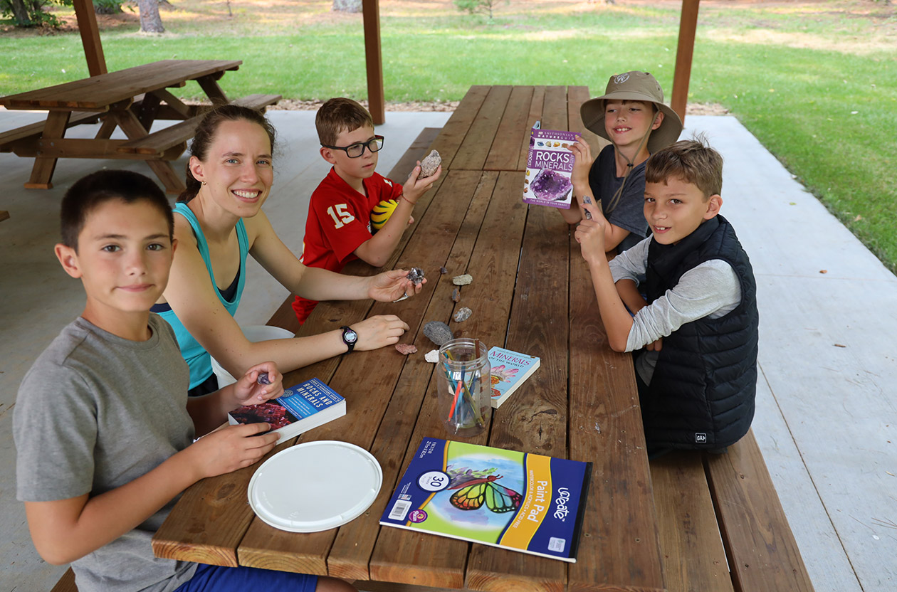 campers looking at rocks and study guides with nature instructor outside.