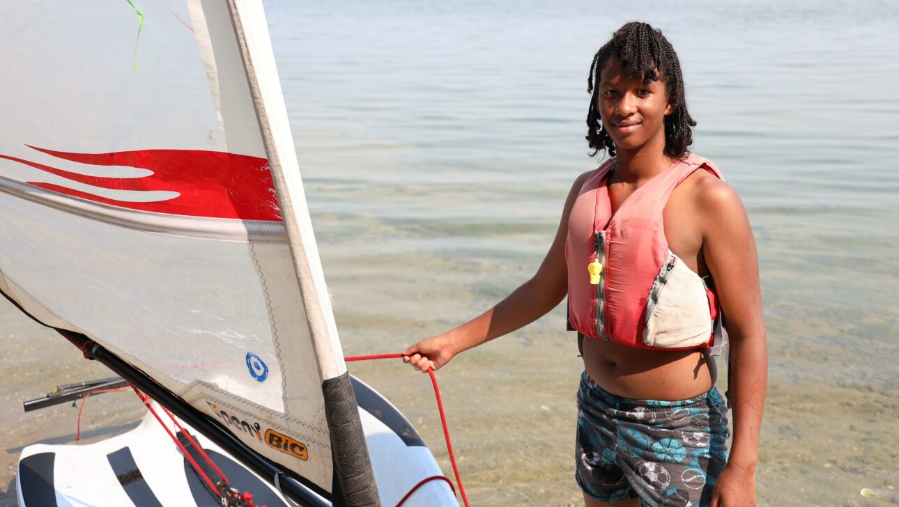 camper standing in the lake with a sail boat.