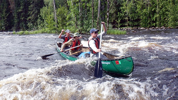 three boys canoeing down rapids