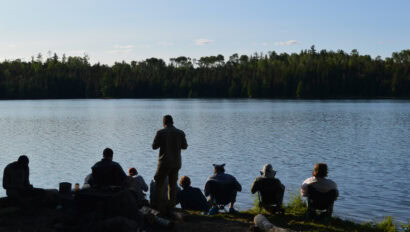 A group of voyageurs sitting on the shore of a lake.