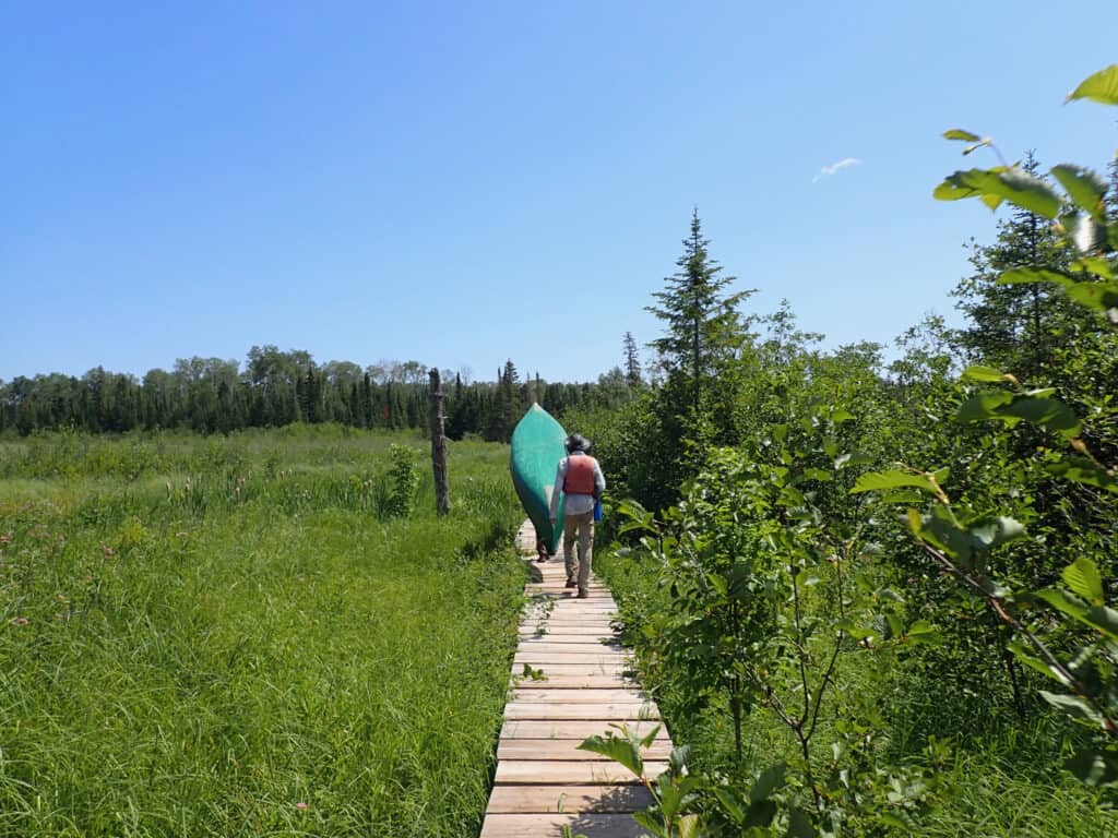Carrying and portaging gear on a boardwalk near the Grand Portage.