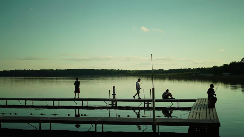Four boys fishing at sunset on a dock by a lake.
