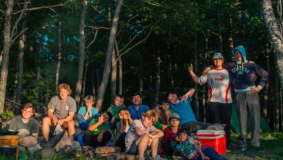 Group of adults and kids posing for a picture around a campsite.